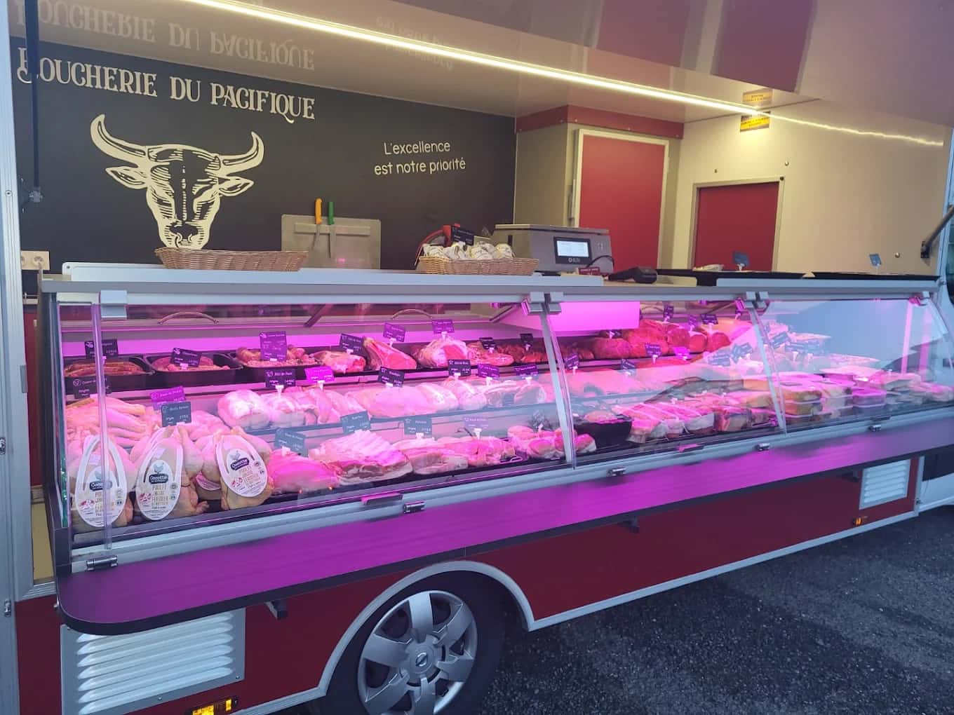 Vitrine réfrigérée du camion-boutique de la Boucherie du Pacifique, garnie de viandes et volailles, éclairée à la tombée de la nuit.